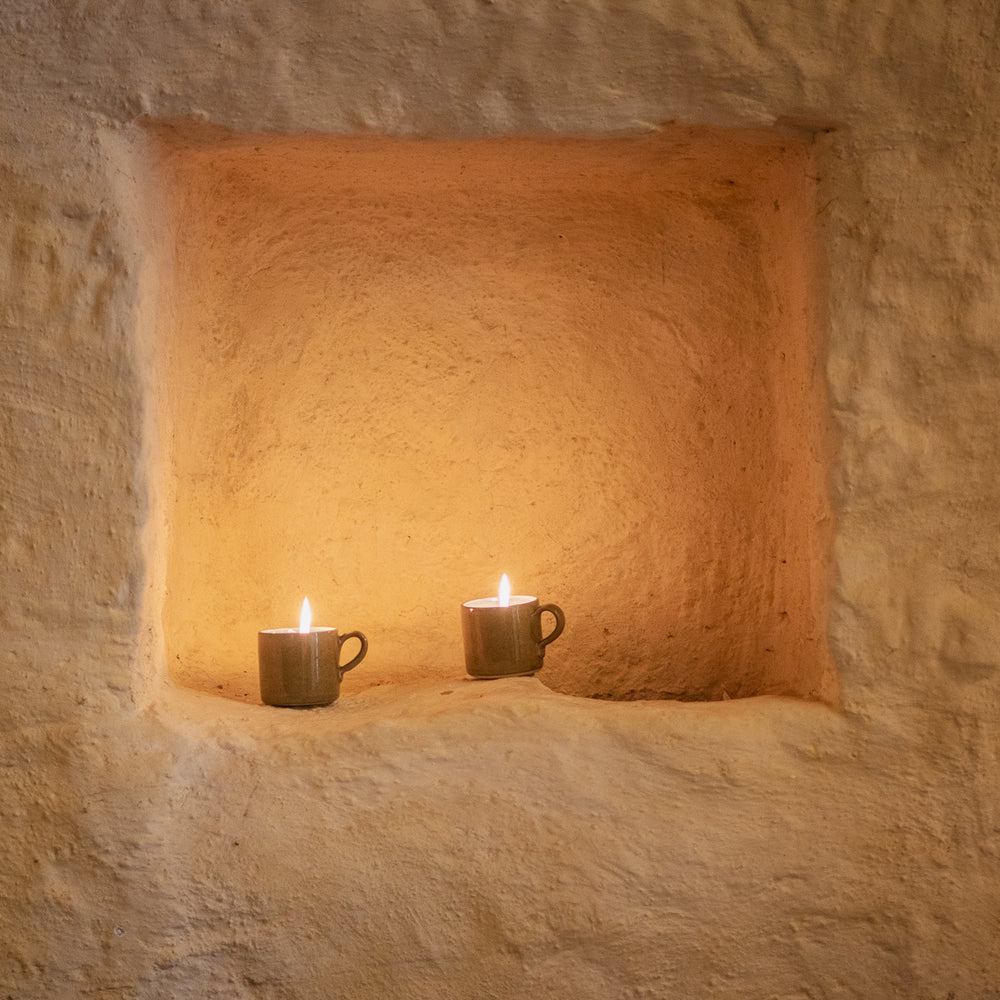 Two lit candles in rustic ceramic cups inside a stone alcove.