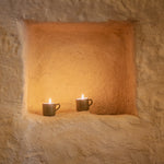 Two lit candles in rustic ceramic cups inside a stone alcove.
